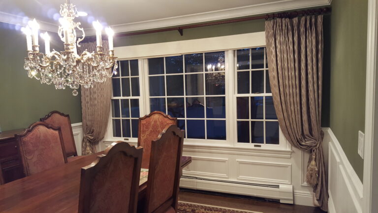 Pinch pleat drapery beside a bay window in a formal dining room with crystal chandelier