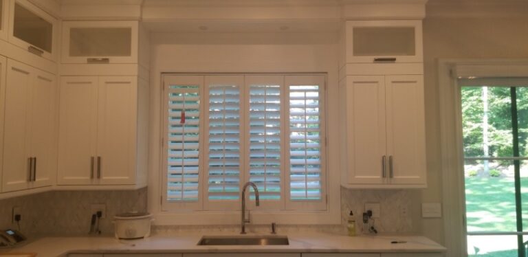 Plantation shutters at a kitchen sink window between white cabinets