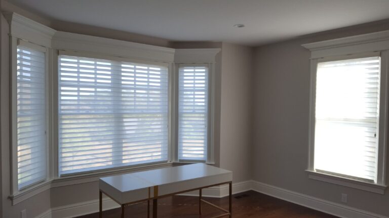 Sheer shades across a faceted bay window in a study with a writing desk