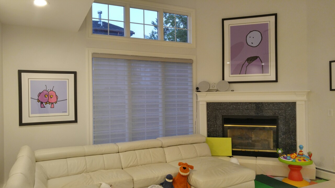 Sheer shades across a wide window beside a marble-front fireplace in a room with white walls, a cream leather sectional and framed prints