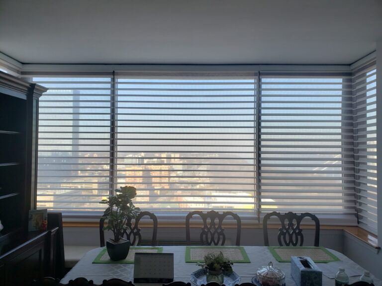 White zebra shades across a wide dining room window with a city view beyond