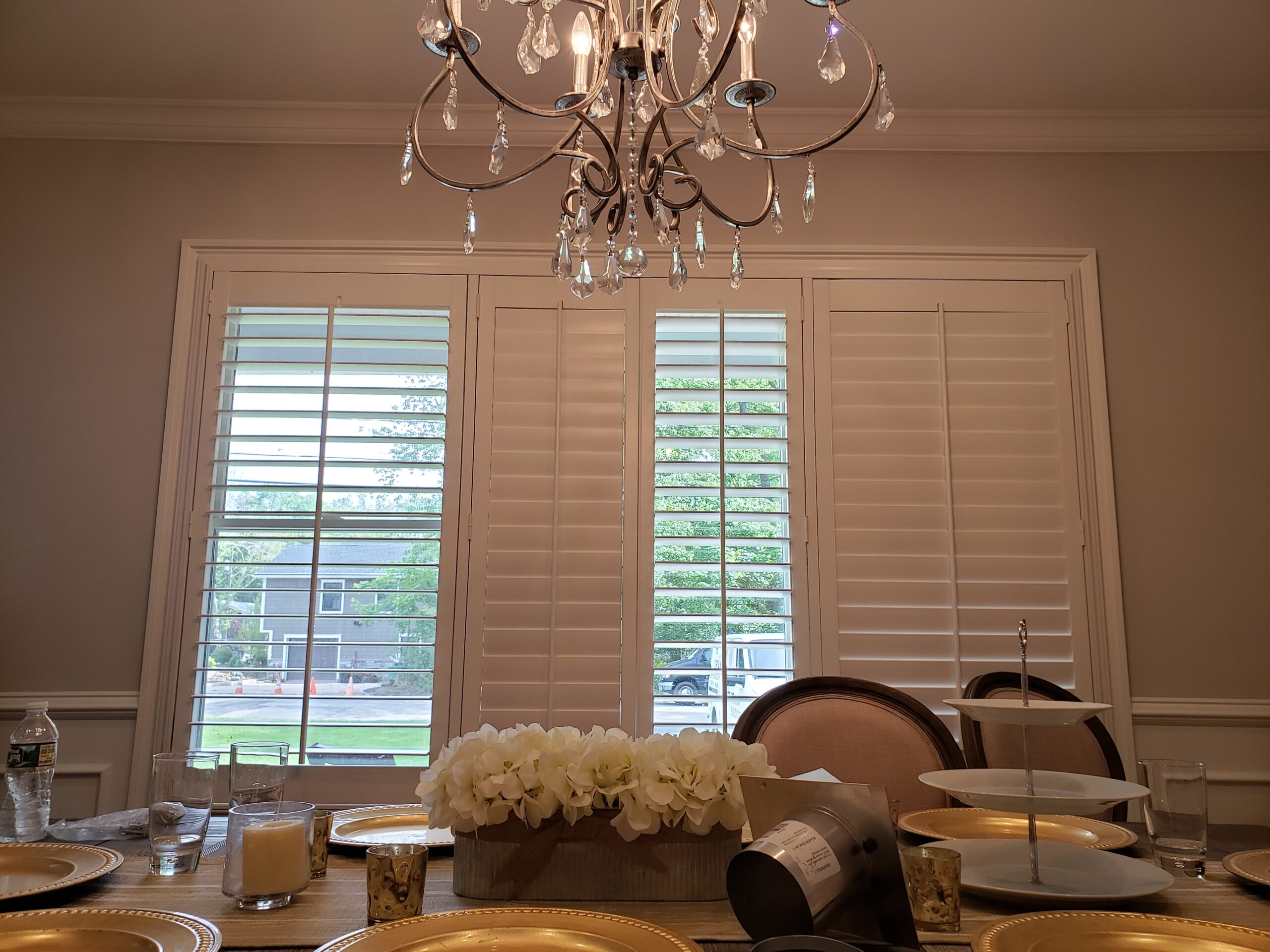 Plantation shutters on dining room windows under a chandelier