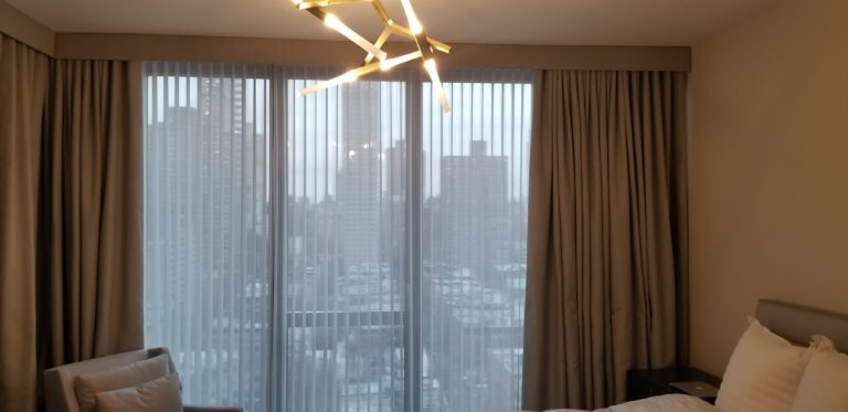 Vertical privacy sheers and drapery panels over a bedroom sliding door with a city skyline view
