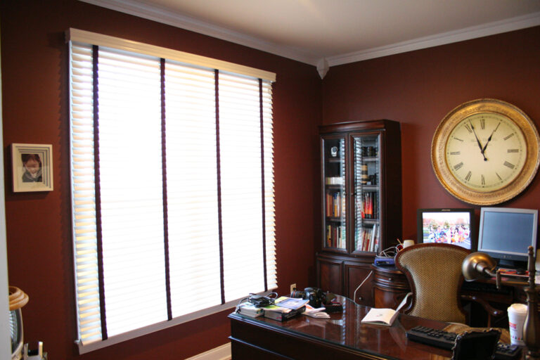 White wood blinds on a wide office window with a traditional desk and wall clock