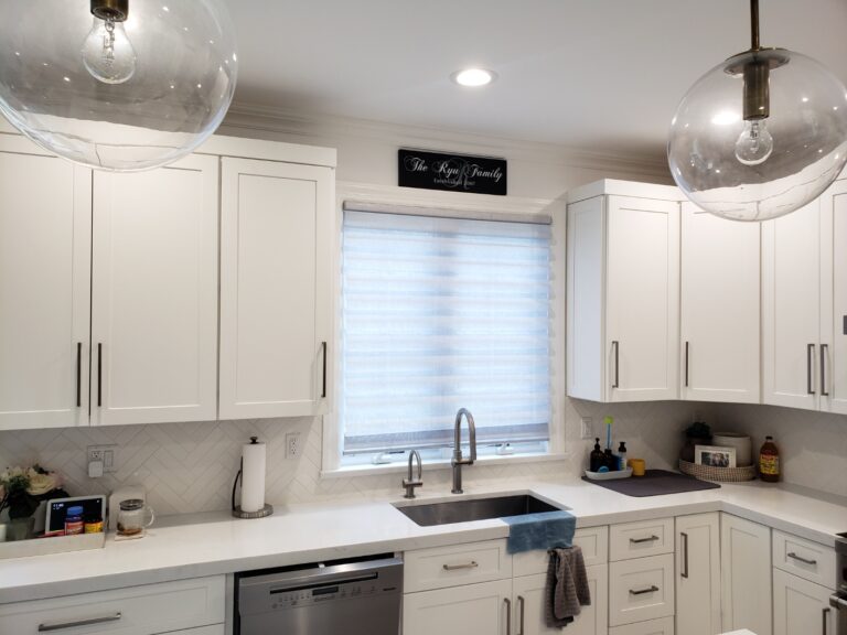 Roman shade over the sink window in a white shaker kitchen with globe pendant lights