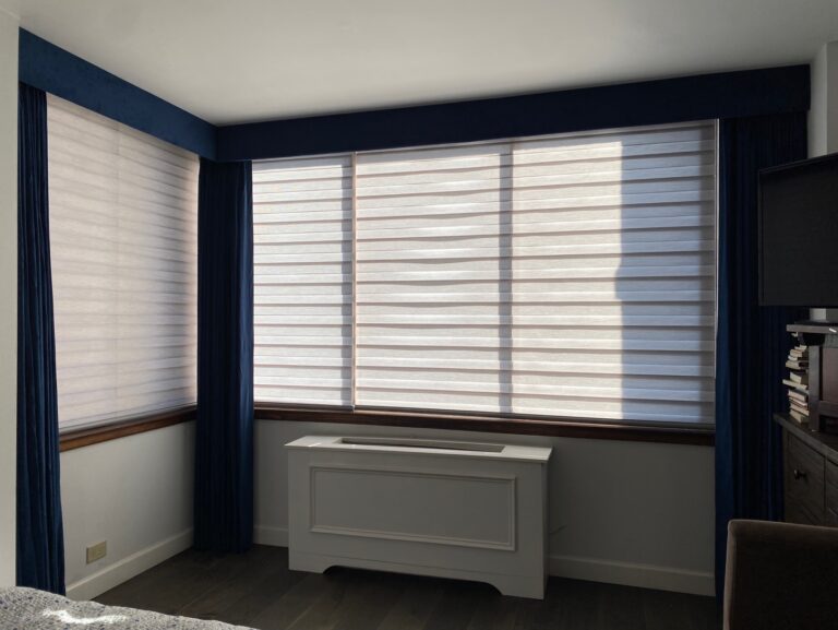 Dual sheer zebra shades across a bay window in a bedroom with navy drapery valance