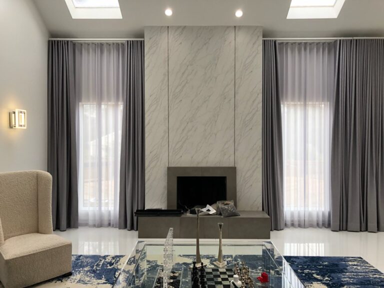 Grey pinch pleat drapery panels flanking a marble fireplace in a modern living room