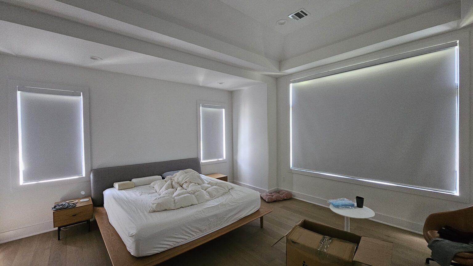 Large white roller shades on two bedroom windows in a bright minimalist bedroom