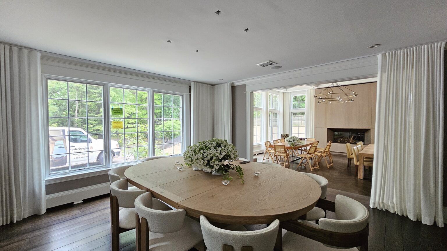 Custom white drapery panels framing floor to ceiling windows in a modern dining room with oval table