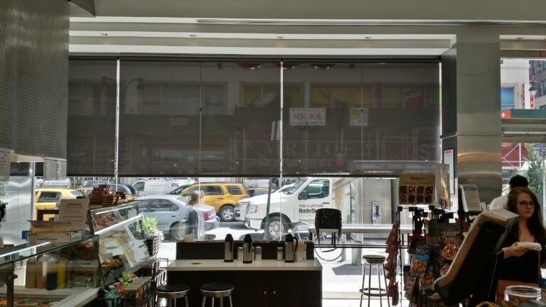 Storm grey solar screen roller shades across a tall commercial window wall