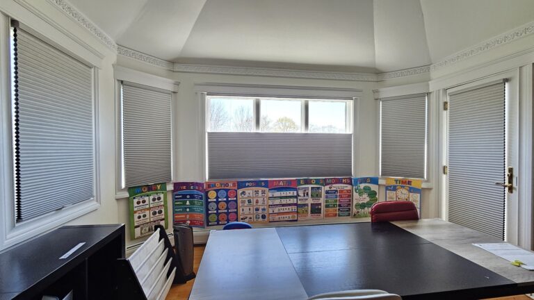 Cellular honeycomb shades fitted across a bay window in a home office