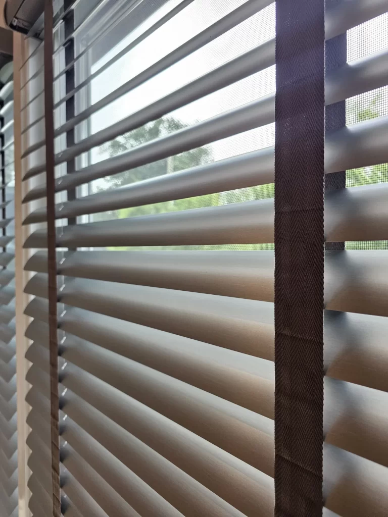 Close-up of thin aluminum blind slats tilted open beside a dark cloth tape