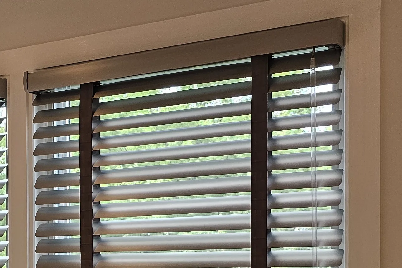 Top of a gray aluminum blind with its matching valance, dark cloth tape and tilt wand