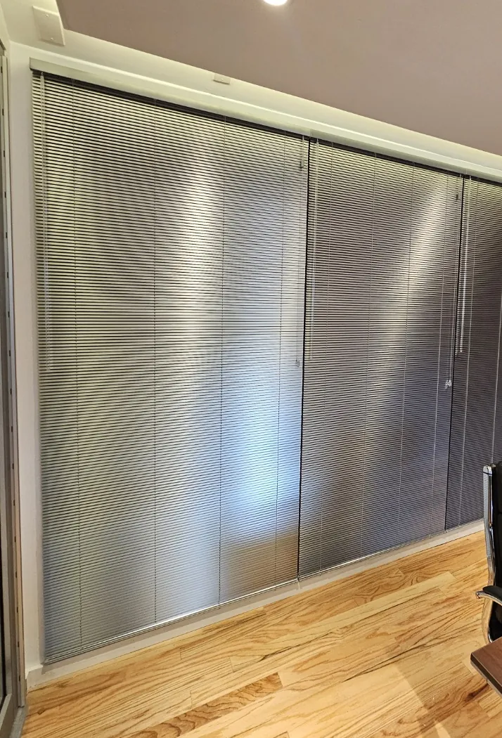 Narrow-slat aluminum mini blinds lowered across a glass wall in a private office