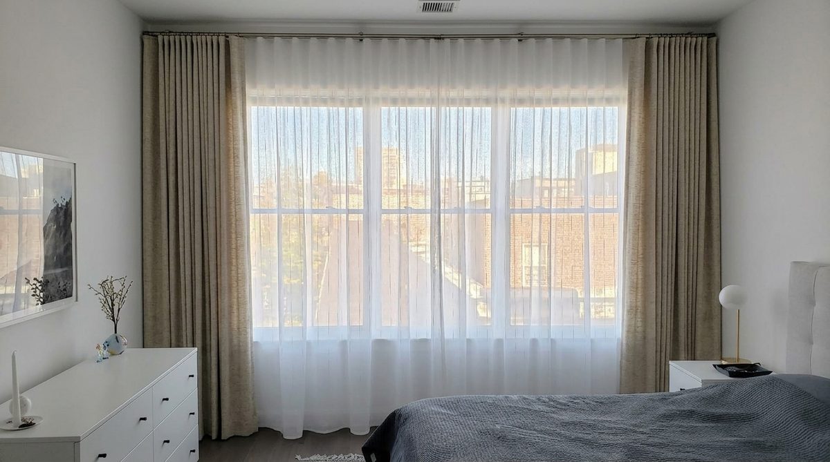 Sheer curtains hung closest to the glass with heavier woven drapery panels stacked open on the outside layer, two distinct layers visible