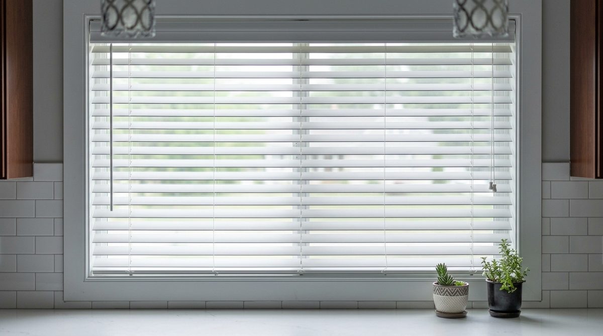 Close view of white faux wood blind slats on a kitchen window, smooth painted composite surface with no grain at all