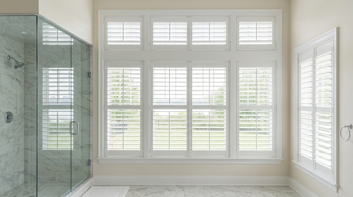 White shutters on a bathroom window immediately beside a tiled shower enclosure, louvers tilted open