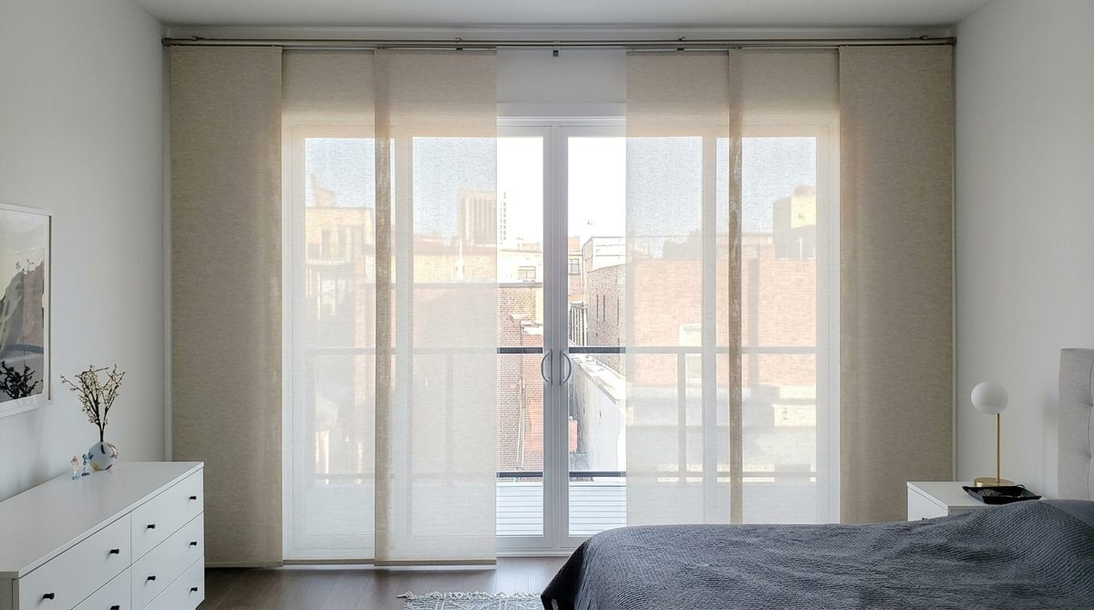 A panel track blind with four wide flat fabric panels sliding across a wide glass door, panels overlapping slightly