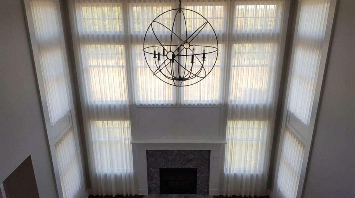 Vertical sheer fabric vanes suspended between two layers of sheer fabric across a tall window, glowing softly with daylight passing through