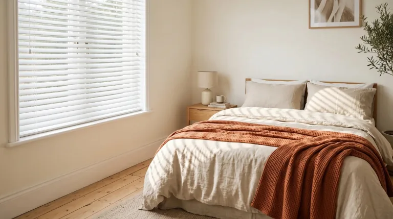 Slim white venetian blinds tilted across a bright bedroom window