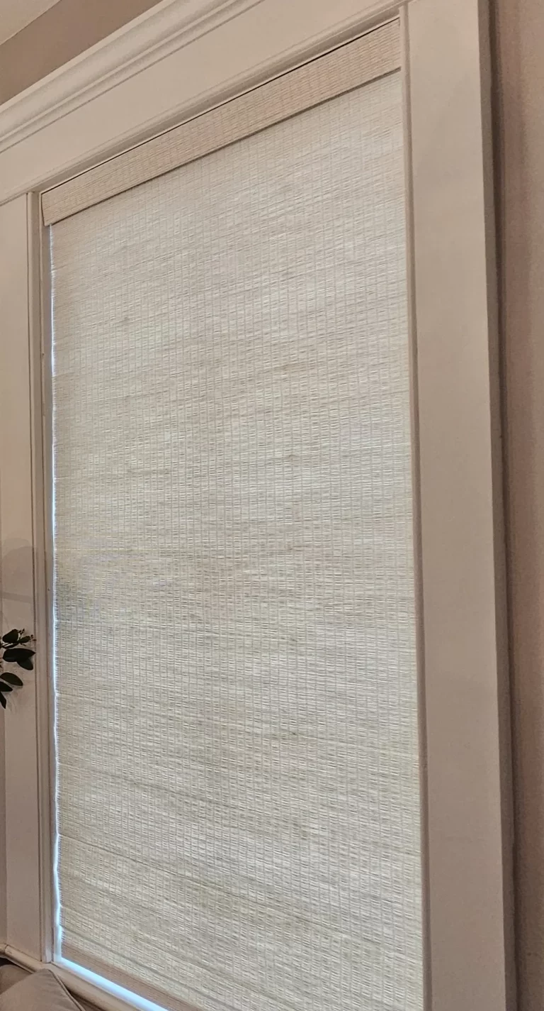 A light natural woven wood shade lowered over a tall window