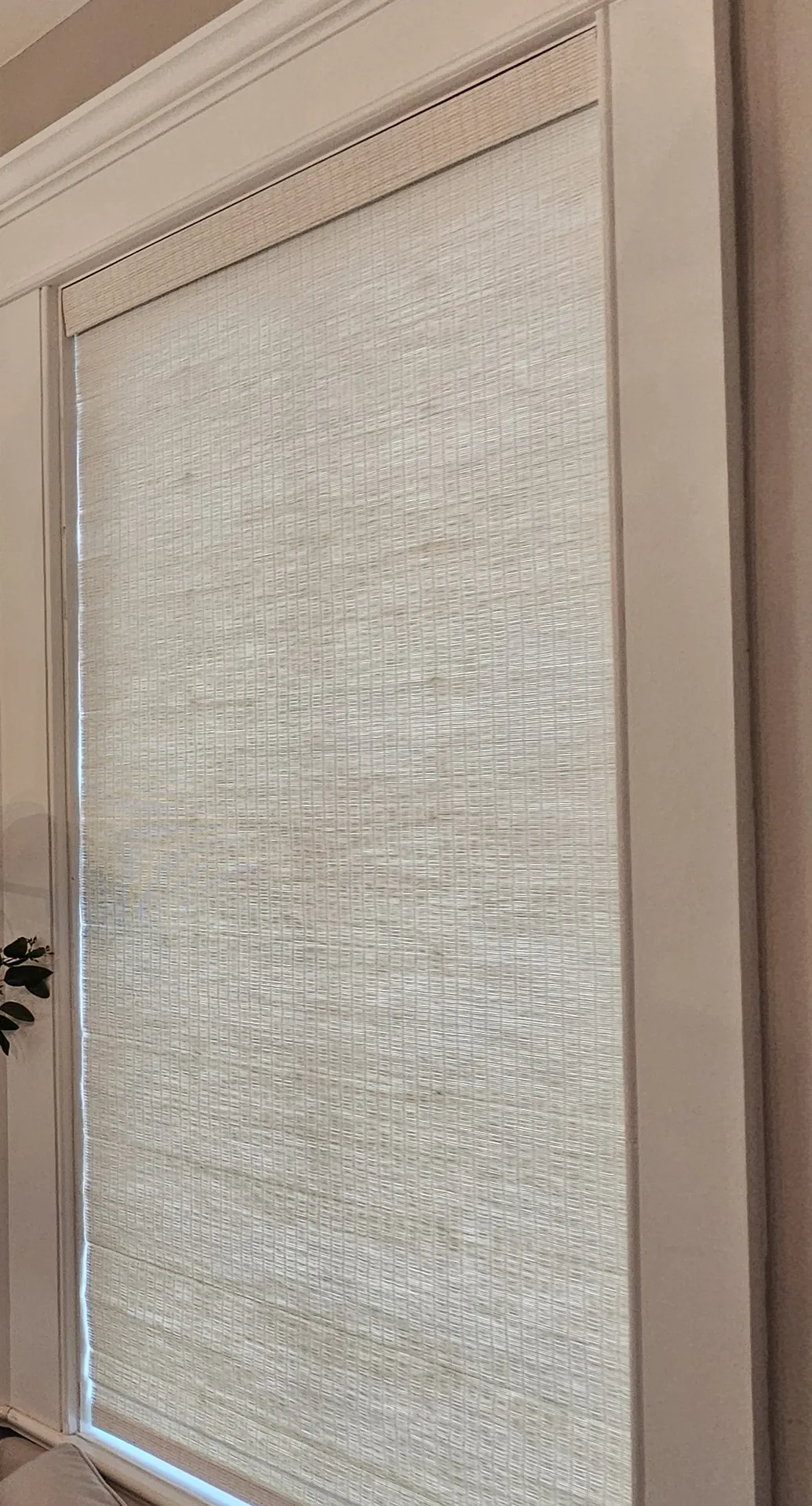 A light natural woven wood shade lowered over a tall window