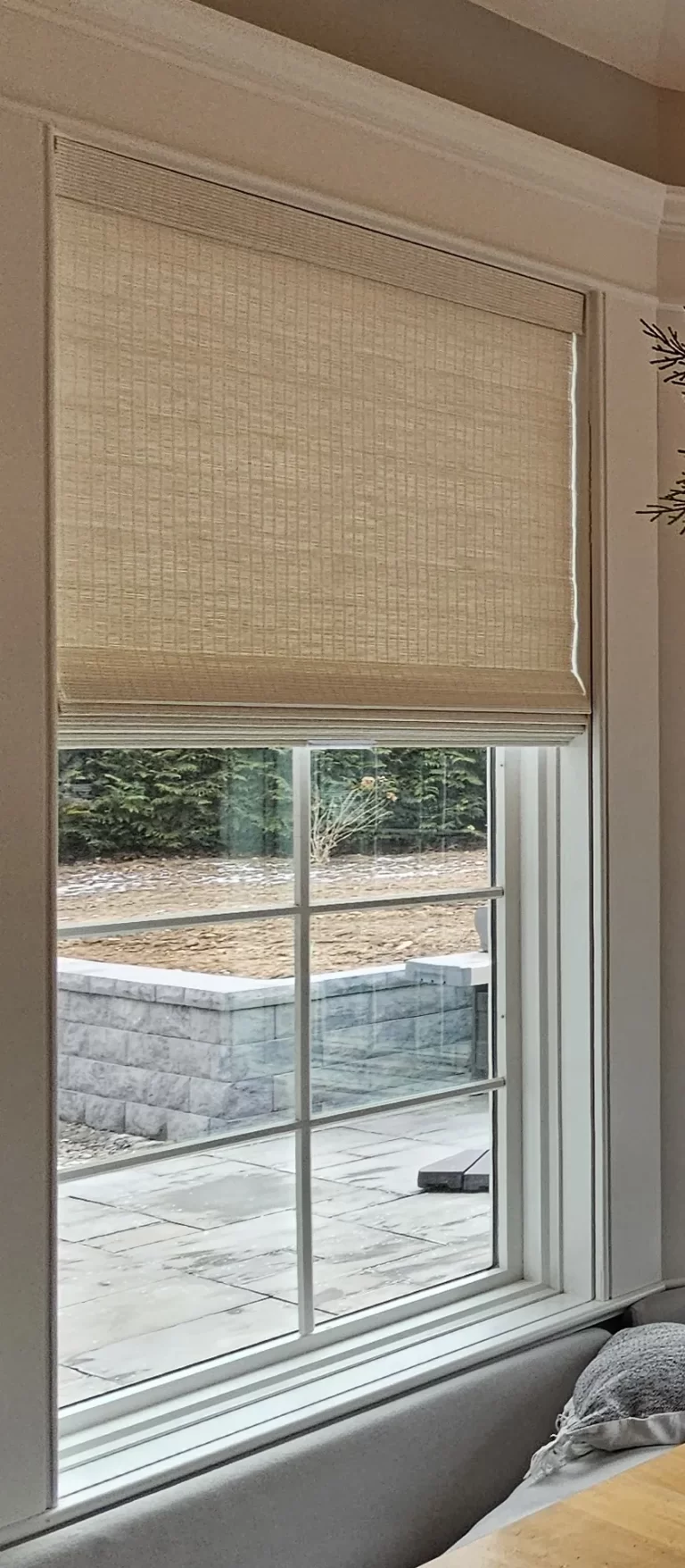 A woven wood shade raised to the top of a divided-light window above a banquette