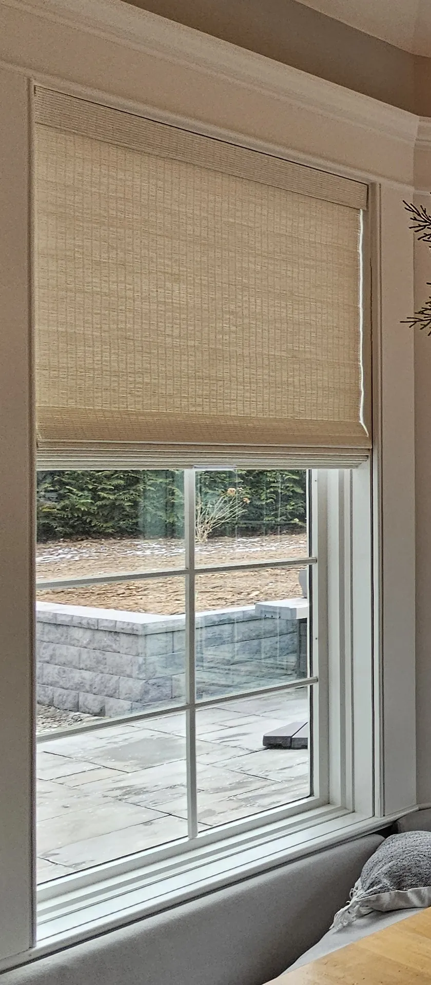 A woven wood shade raised to the top of a divided-light window above a banquette