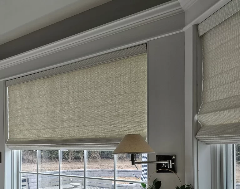 A woven wood shade raised above a large picture window with a second shade on the window beside it