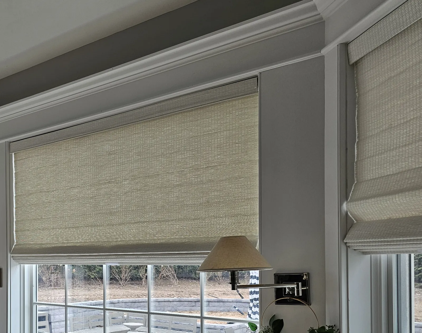 A woven wood shade raised above a large picture window with a second shade on the window beside it