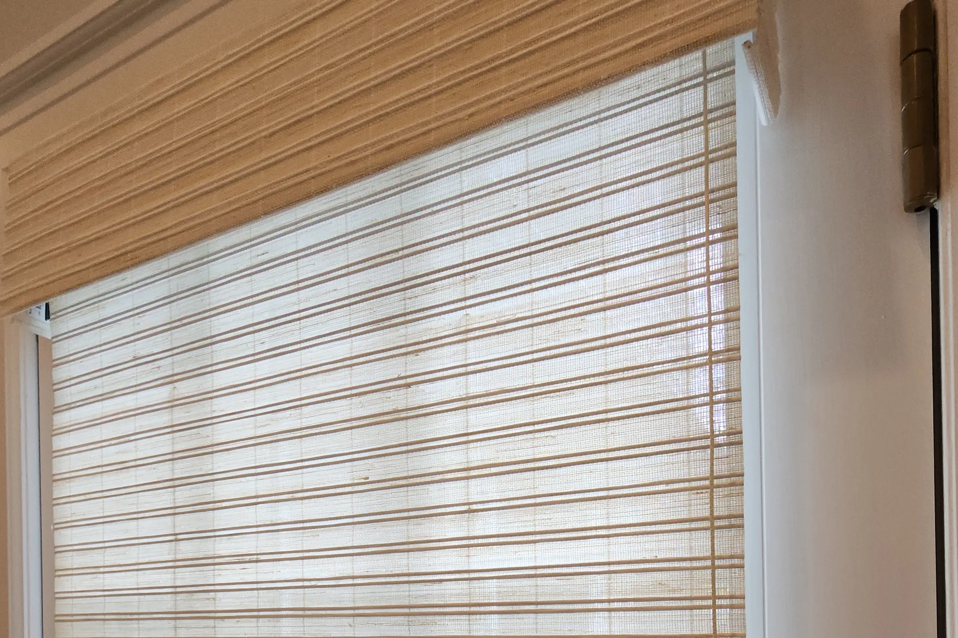 A natural woven wood shade partly raised on a door window, with daylight showing through the weave
