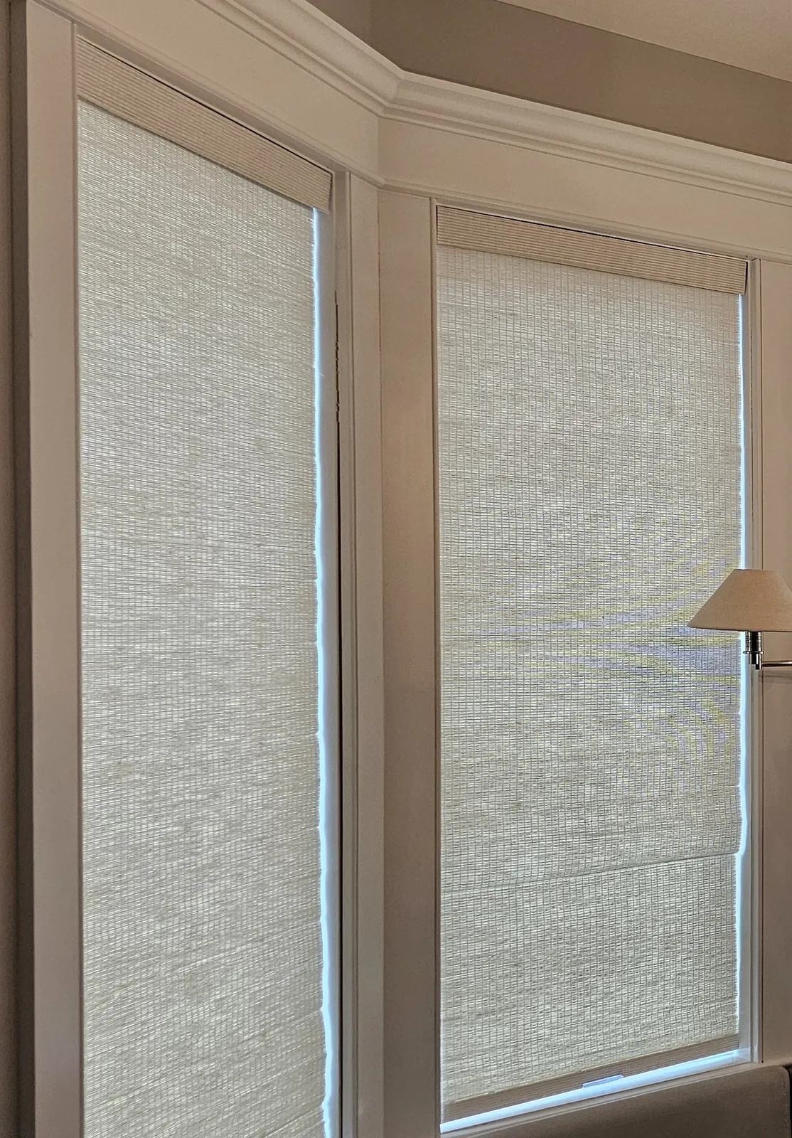 Woven wood shades lowered on two angled windows of a bay, softening the daylight
